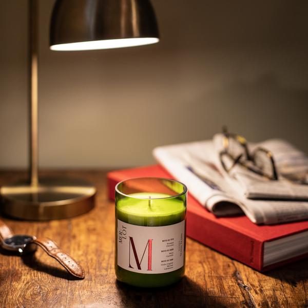 Duftkerze Merlot steht auf einem Holztisch mit einem Buch, eine Tischlampe, eine Uhr und Zeitungen